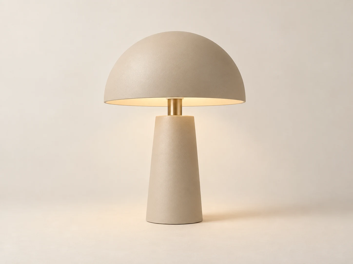 Lampa stołowa w piaskowym kolorze, z zaokrąglonym kloszem i ciepłym światłem.